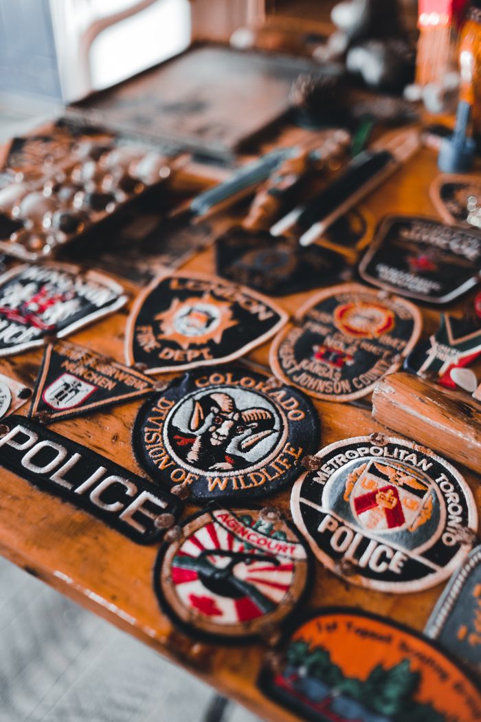 about-img-02 Collection of diverse police and security badges displayed on a wooden table surface.